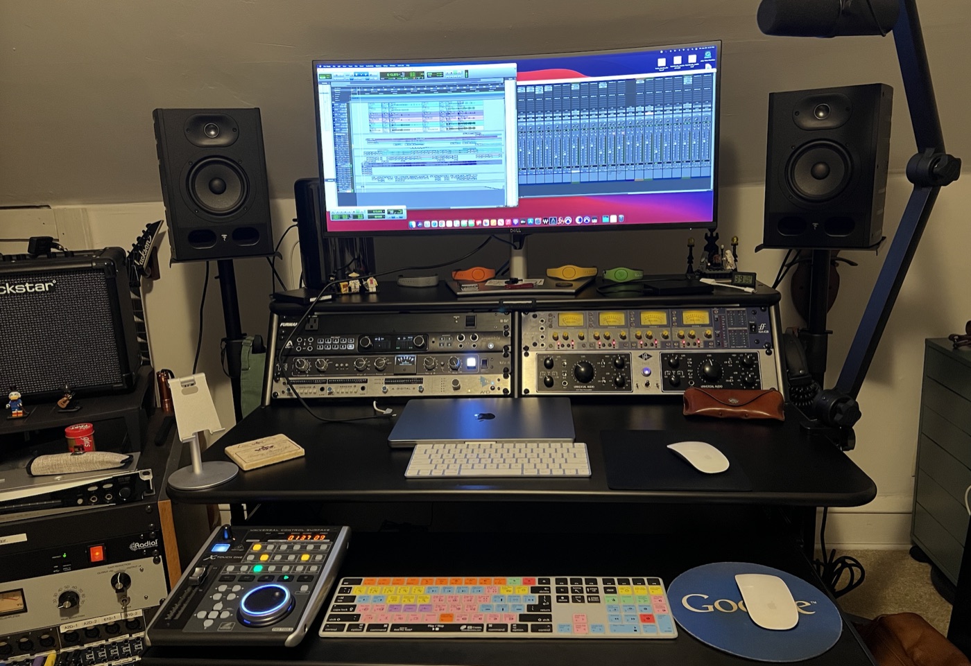 DAW workstation with large monitor displaying a mix session, outboard gear rack, and Focal studio monitors