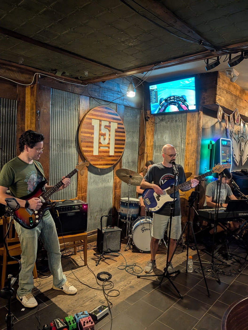 Band performing live at a venue — guitar, bass, drums, and keyboards on stage