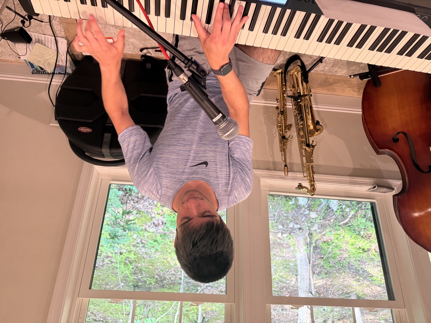 Student at a Roland keyboard with condenser microphone, saxophone and upright bass visible in the background